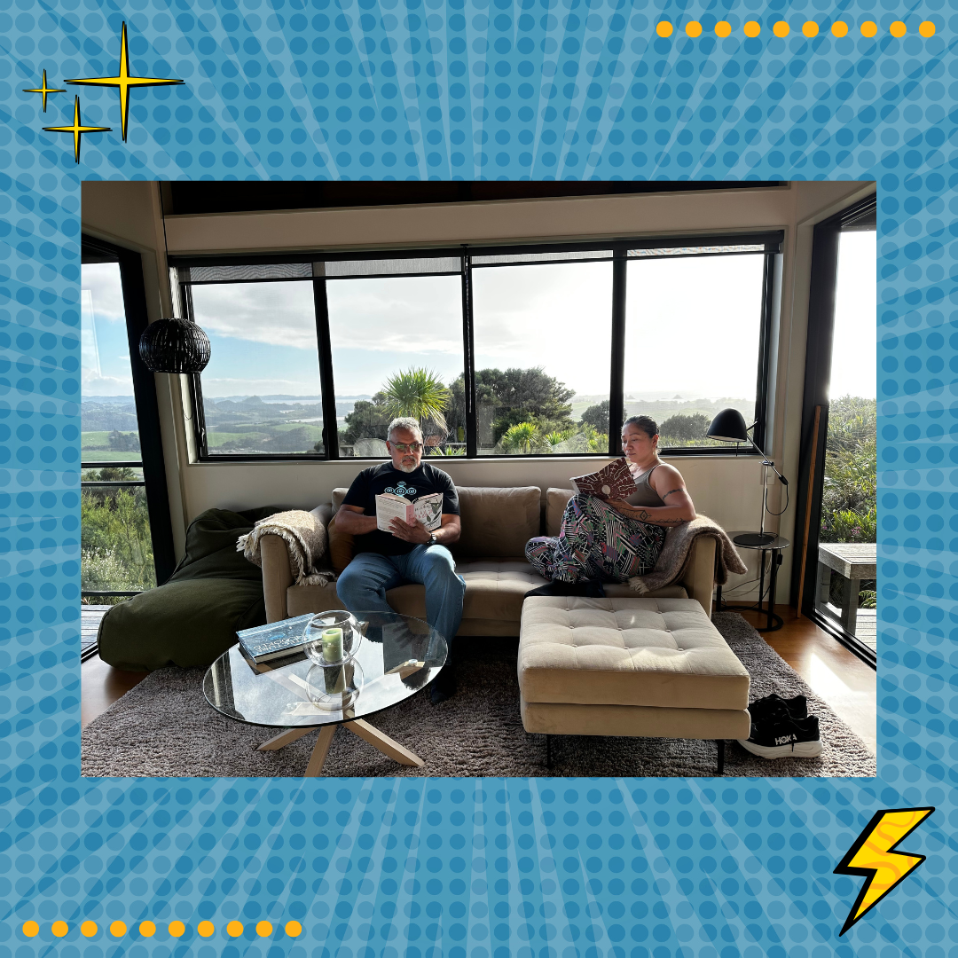 Mark Yettica-Paulson and Maryann Talia Pau reading together in a sunlit living room with panoramic views of nature, featured on Damper & Fetū lifestyle blog.