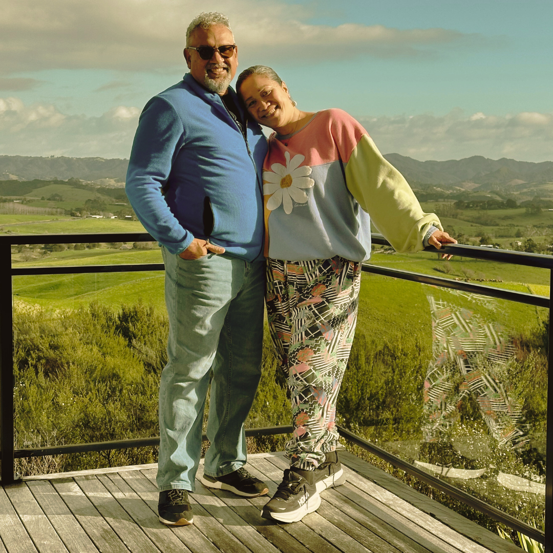 Mark Yettica-Paulson and Maryann Talia Pau standing together overlooking lush countryside, Indigenous leadership and weaving arts duo.