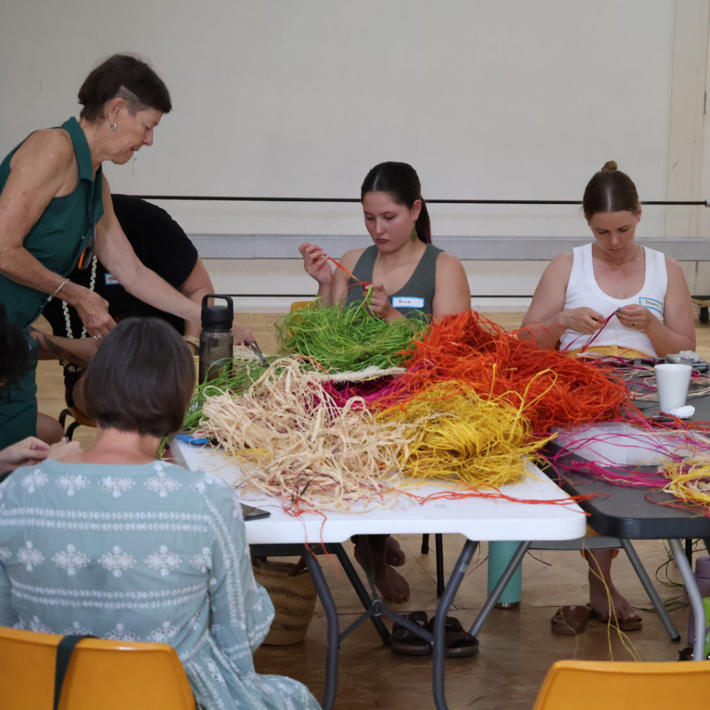 Women sitting and learning to weave their own earrings with Maryann Talia Pau